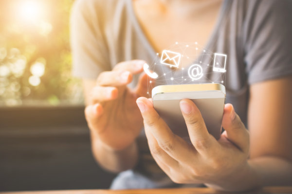 A women holding a phone in the palm of her hand with symbols representing various forms of communications hovering over it; email, sms, call.